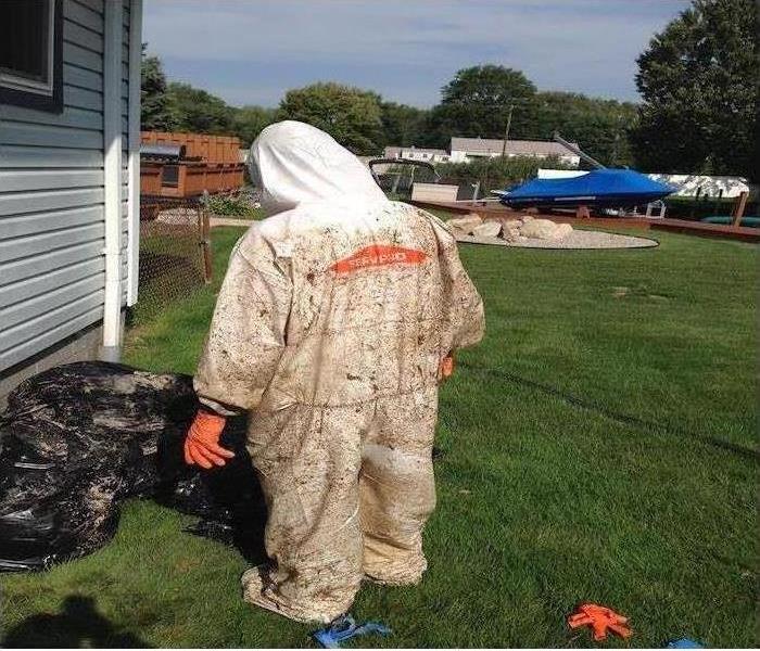 SERVPRO team member in a PPE suit, restoring a damaged home.