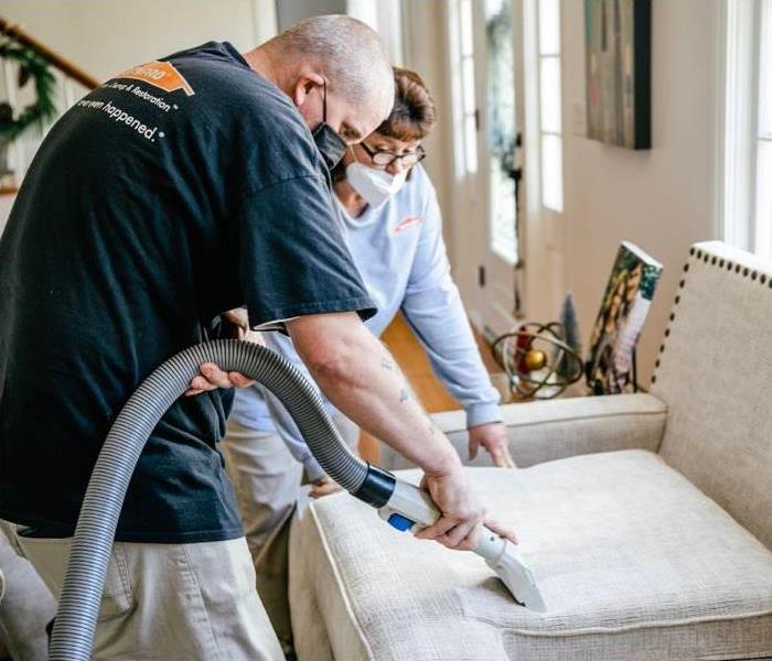 Two SERVPRO workers wearing masks cleaning upholstery in a client's home. 