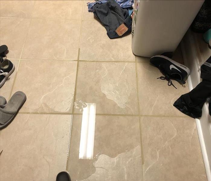 Water puddled up on tile floor with wet clothes and shoes 